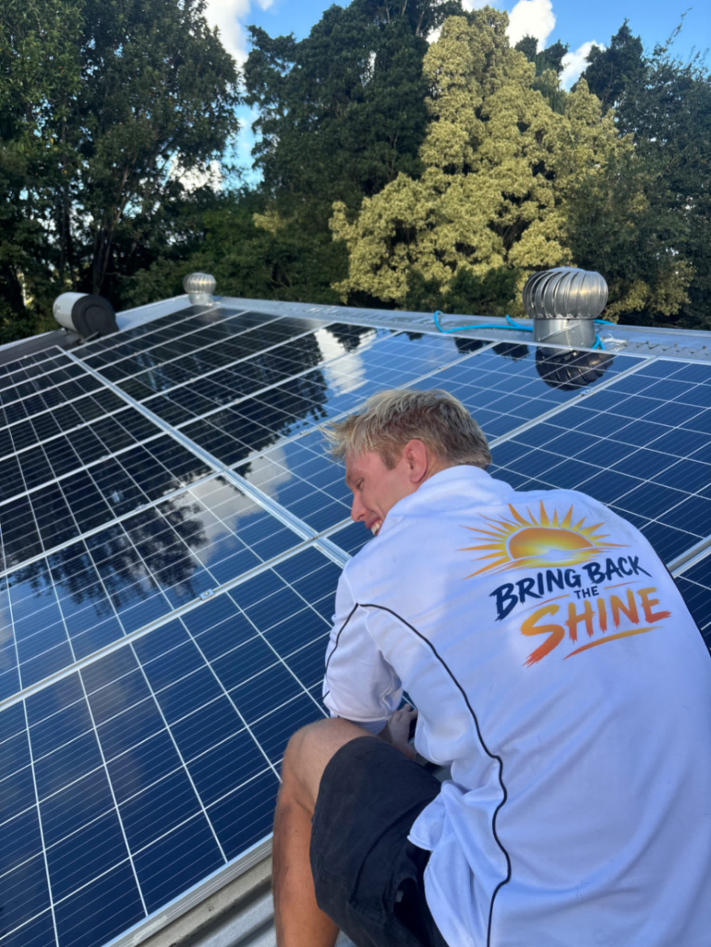 Sunny Scrubbers technician in a Bring Back the Shine shirt cleaning solar panels on a Sunshine Coast roof
