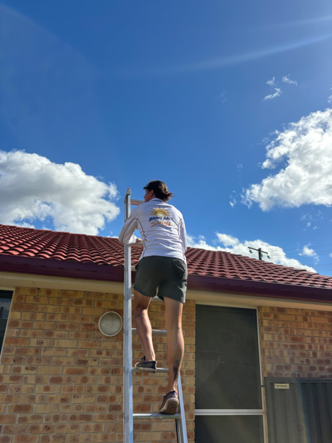 Sunny Scrubbers crew up a ladder clearing the gutters of a Queensland home